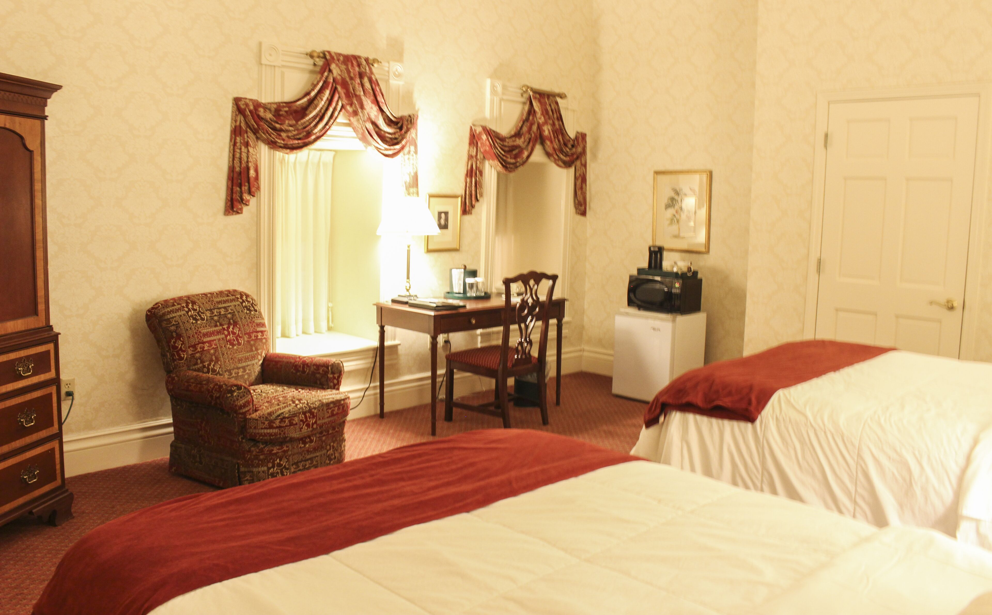 A hotel room with two beds, a desk with a chair, a dresser, and a microwave.