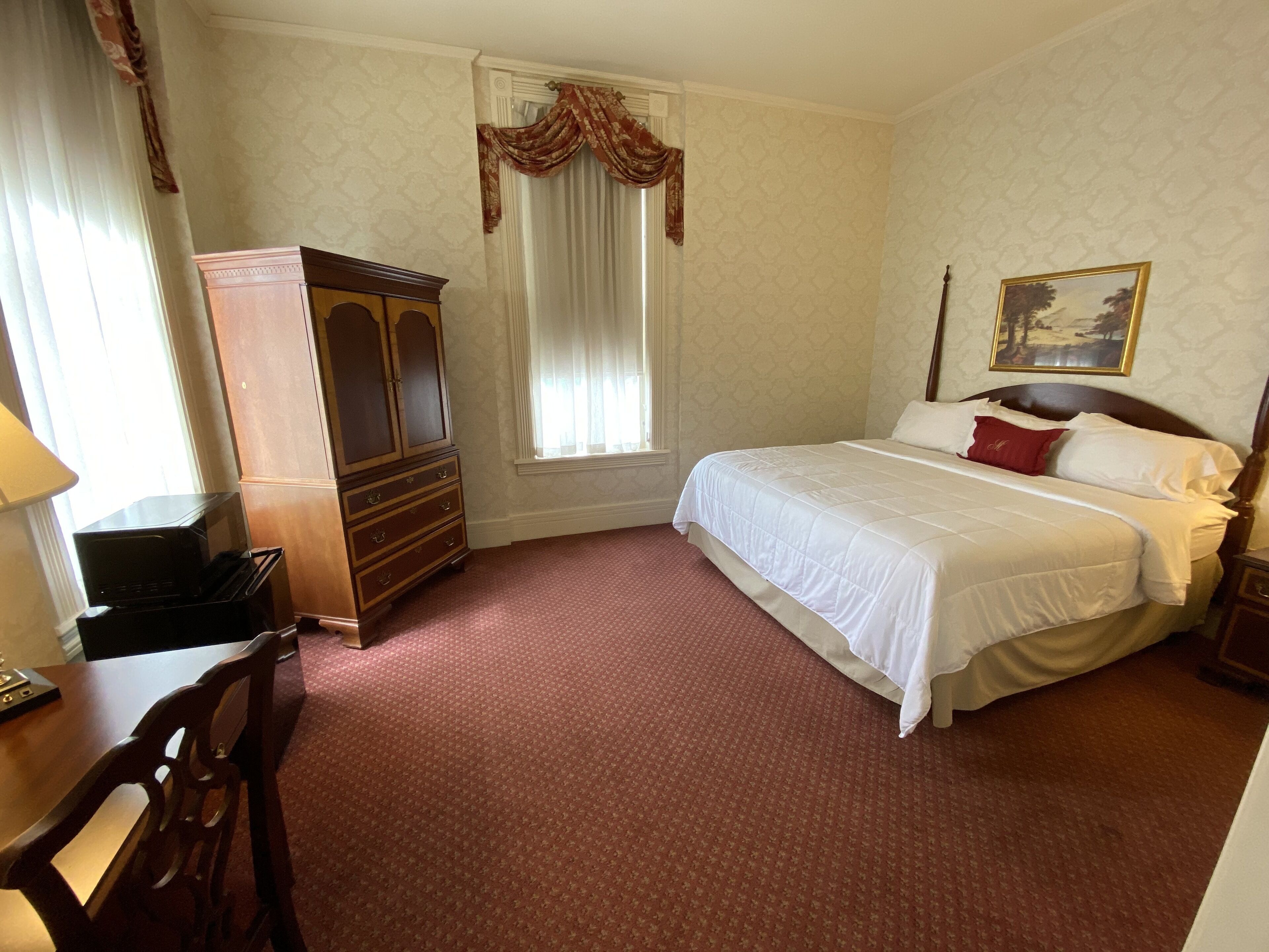 A bedroom with a bed, a wooden dresser, a desk, and a window with curtains.