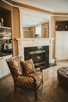 A living room with a fireplace, a wooden chair with patterned cushions, and a bar area with glasses and bottles.