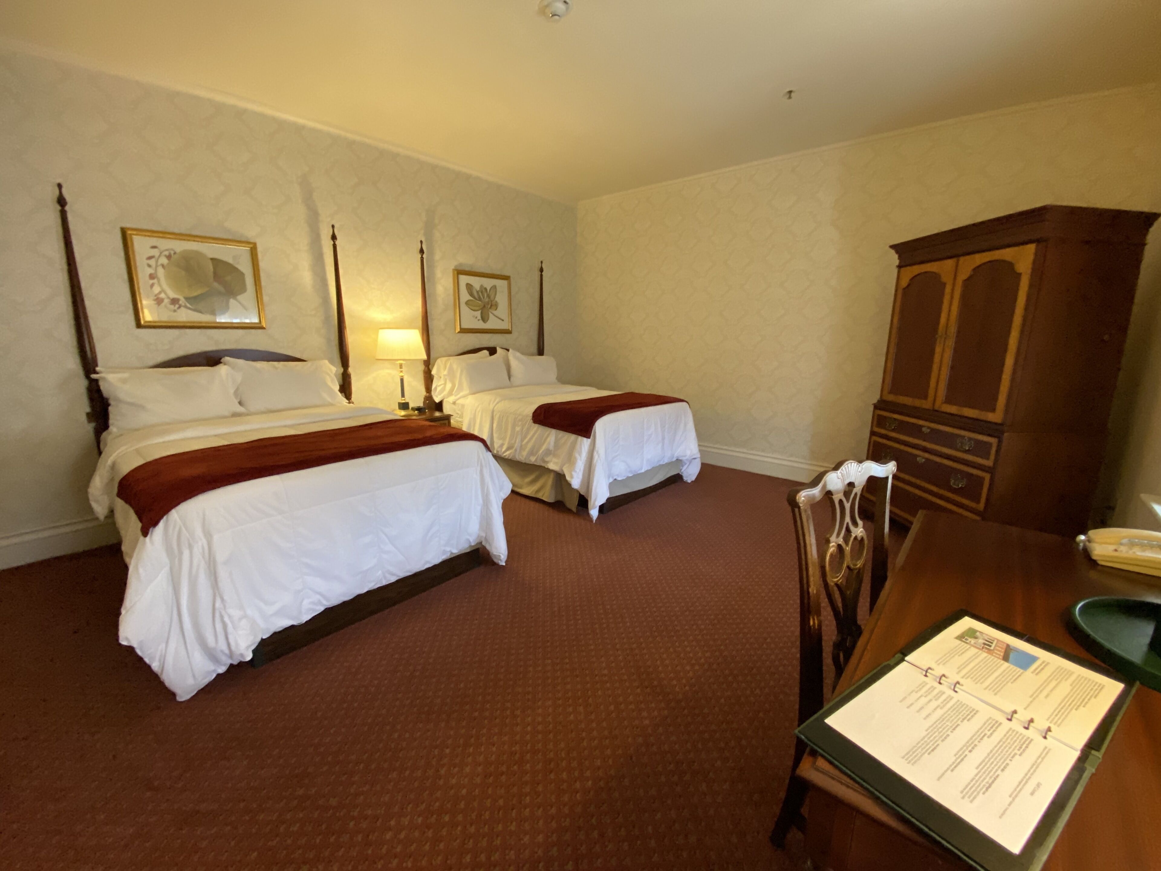 Quarto de hotel com duas camas, um armário de madeira e uma mesa de jantar com um menu.