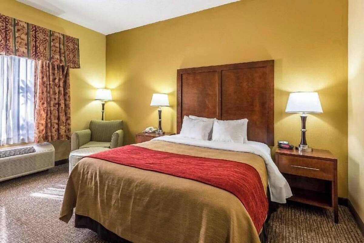A hotel room with a large bed, two bedside lamps, a chair, a nightstand, and a window with curtains.