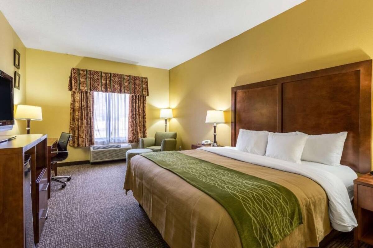 A hotel room with a bed, desk, chair, and two lamps.