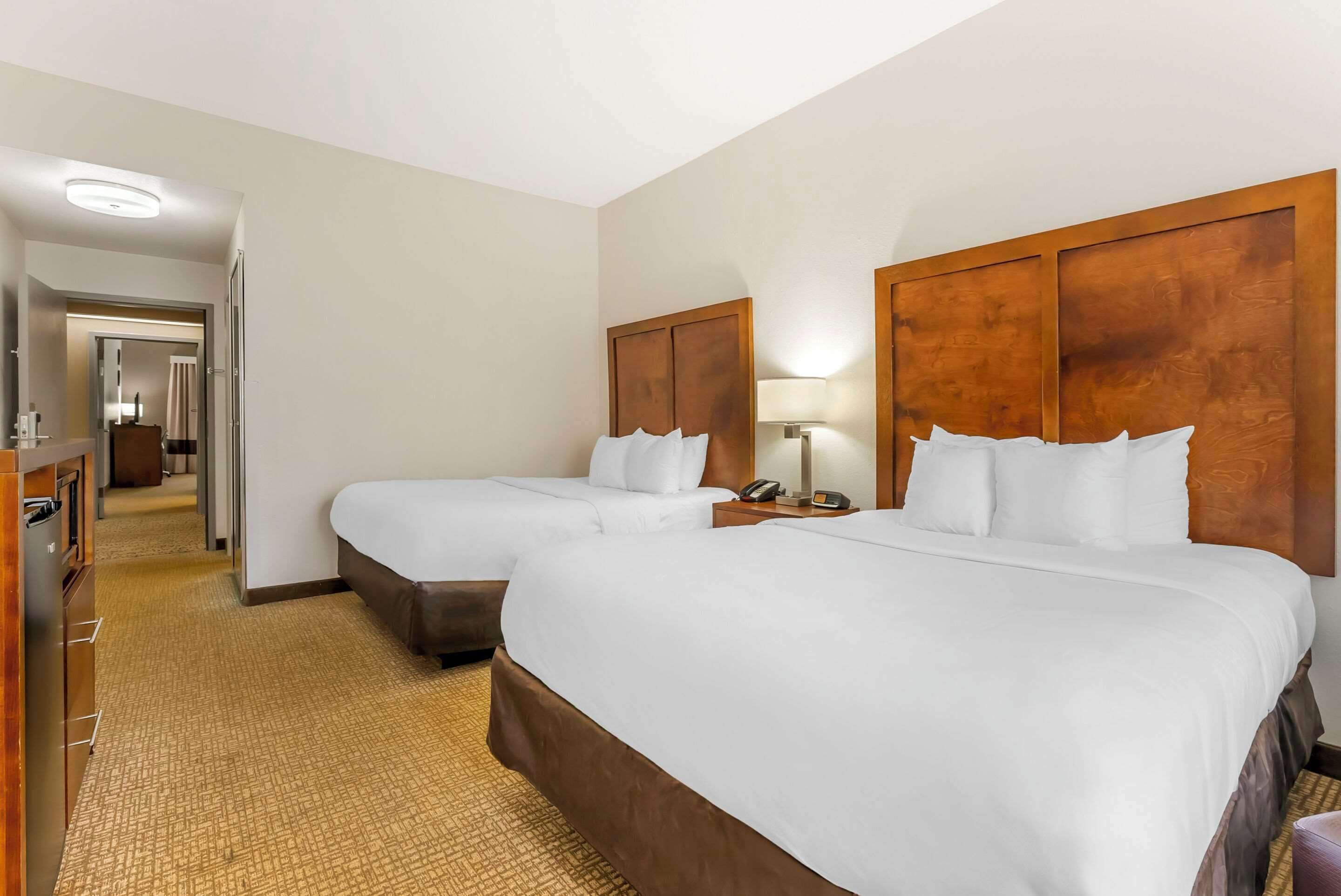 A hotel room with two beds, a wooden headboard, a bedside lamp, a telephone, and a carpeted floor.