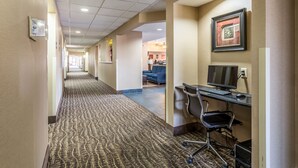 A hotel corridor with a carpeted floor, a reception desk, a computer station, and a framed picture on the wall. - Comfort Inn Brownsville I-40 (Brownsville)