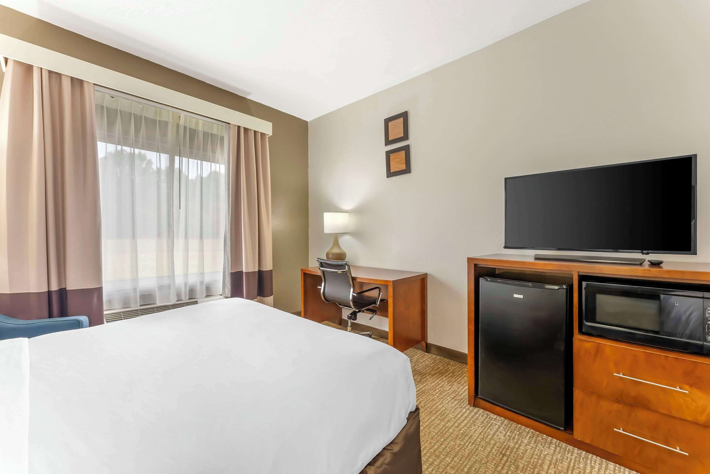 Une chambre d’hôtel équipée d’un lit, d’un bureau avec une chaise, d’une télévision, d’un réfrigérateur et d’un four à micro-ondes.