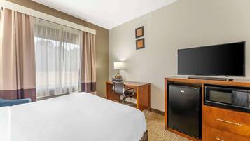 Une chambre d’hôtel équipée d’un lit, d’un bureau avec une chaise, d’une télévision, d’un réfrigérateur et d’un four à micro-ondes.