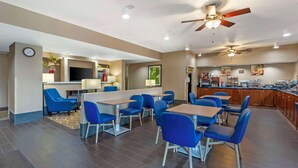 A hotel dining area with blue chairs and tables, a clock on the wall, and ceiling fans. - Comfort Inn Brownsville I-40 (Brownsville)