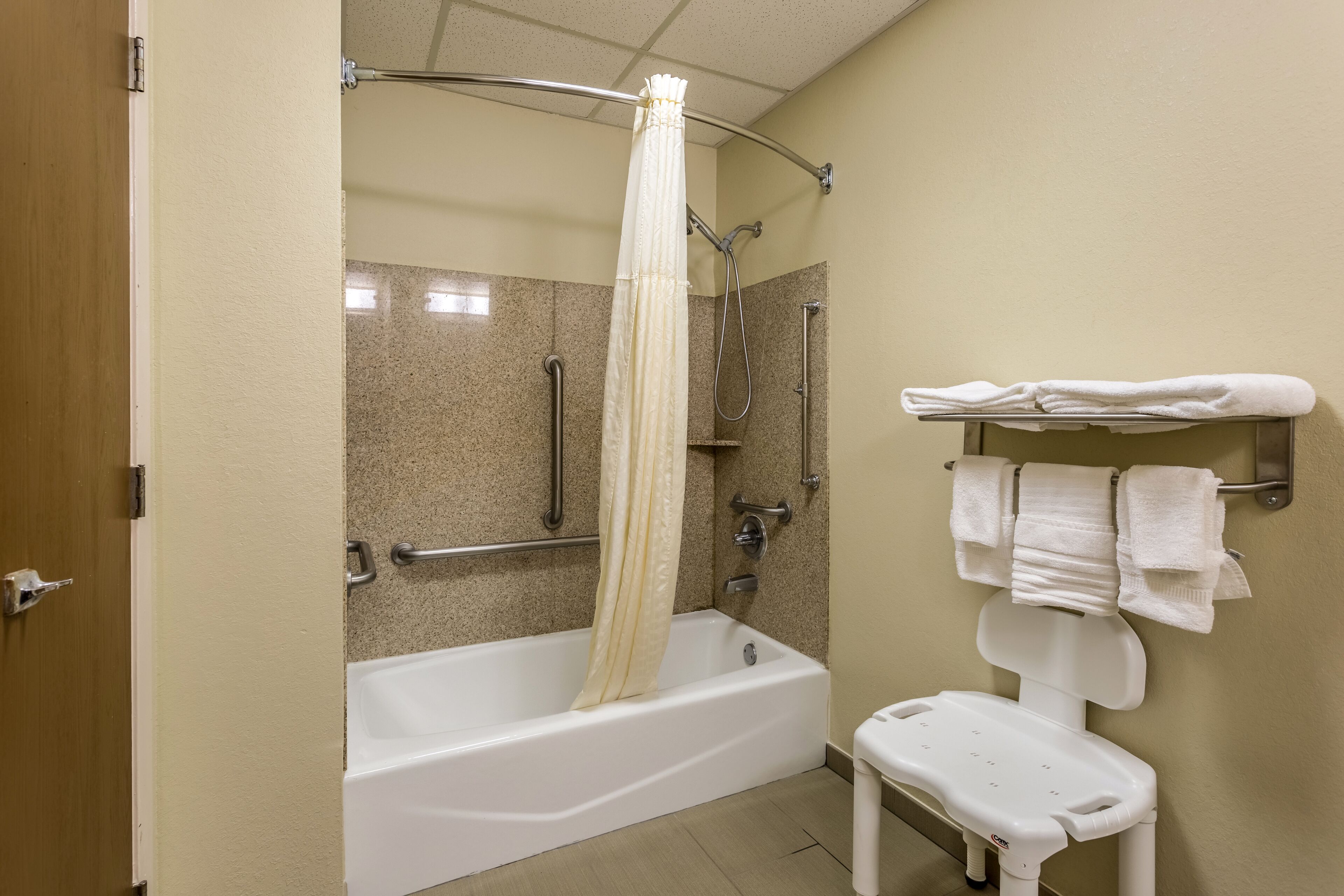 Ein Badezimmer mit Badewanne, Dusche, einer Haltestange, einer weißen Bank und einem Handtuchhalter.