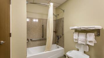Un baño con bañera, ducha, barra de apoyo, banca blanca y toallero.