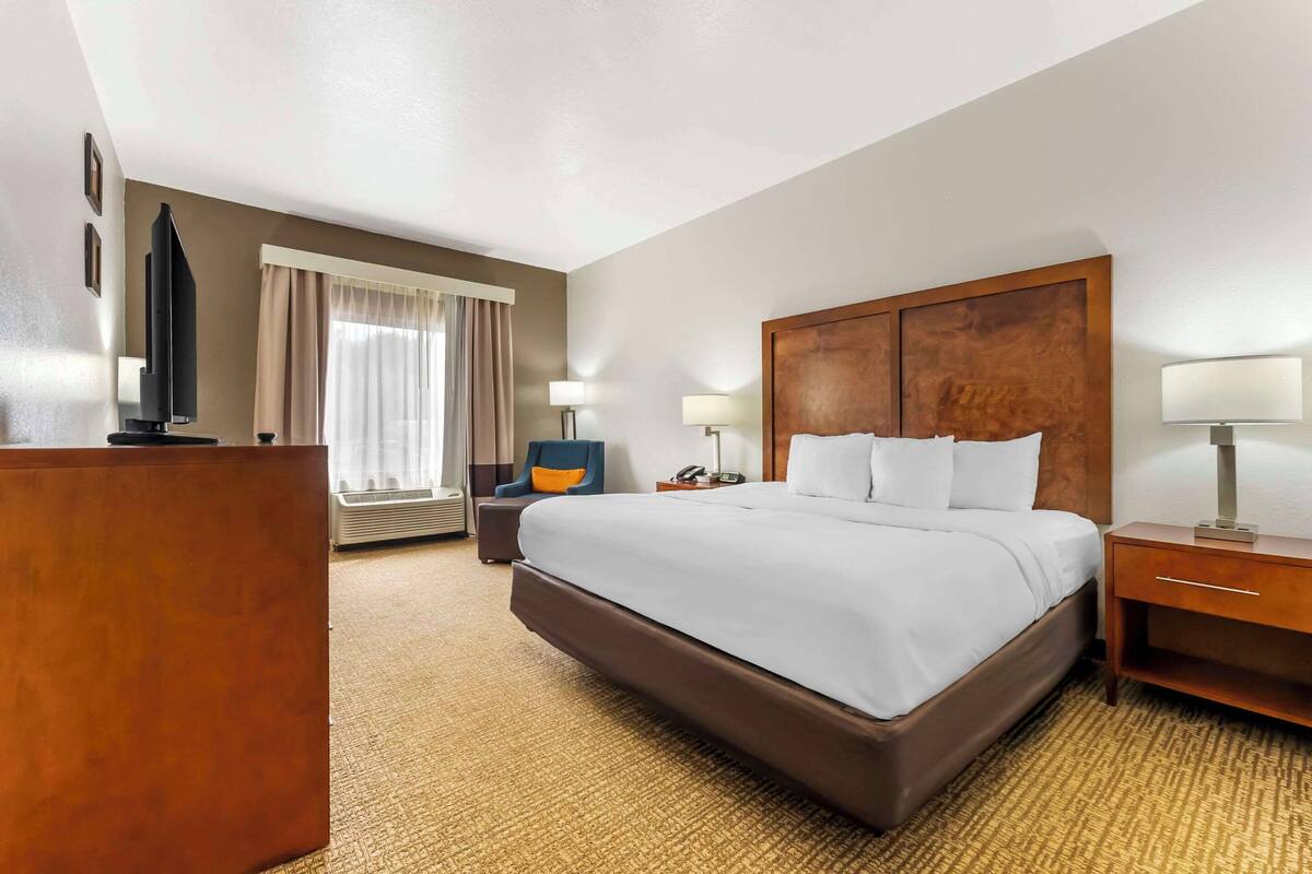A hotel room with a large bed, a desk, a chair, and a TV.