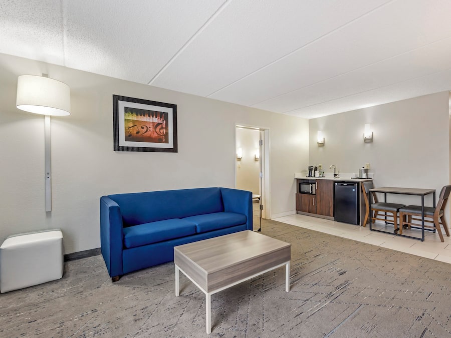 Ein modernes Hotelzimmer mit einem blauen Sofa, einem kleinen weißen Tisch, einer Küchenzeile mit Esstisch und einem gerahmten Bild an der Wand.