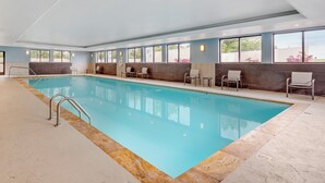 Une piscine intérieure à l’eau d’un bleu limpide, entourée d’espaces aménagés pour s’asseoir et dotée de grandes fenêtres.