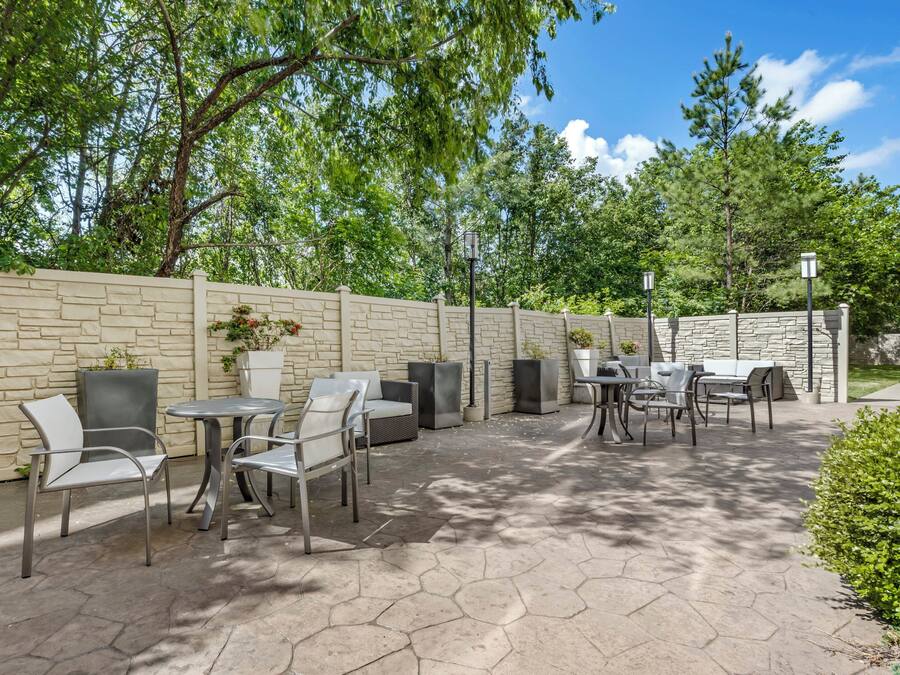 An outdoor patio with stone flooring, metal chairs, a table, and a stone wall.