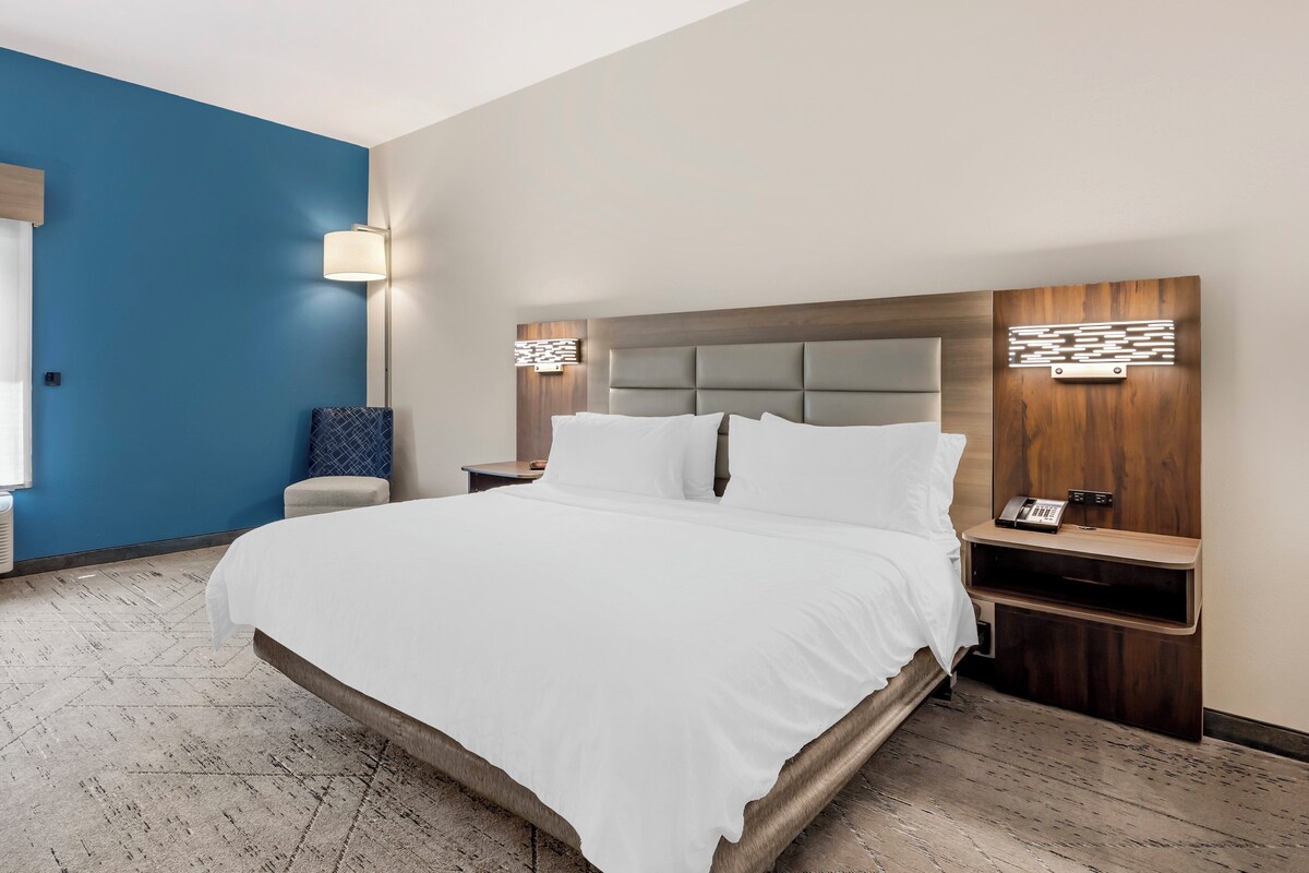 Une chambre d’hôtel moderne avec un grand lit, deux tables de chevet, une petite table et un téléphone fixé au mur.