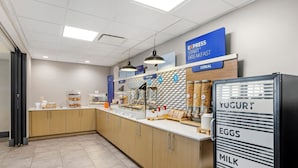 Een ontbijtruimte met een dispenser voor yoghurt, eieren en melk, een bordje voor Express Ontbijt, en een balie met diverse etenswaren.