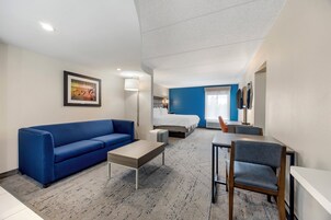 A modern hotel room with a blue sofa, a bed, a small table, and a chair.