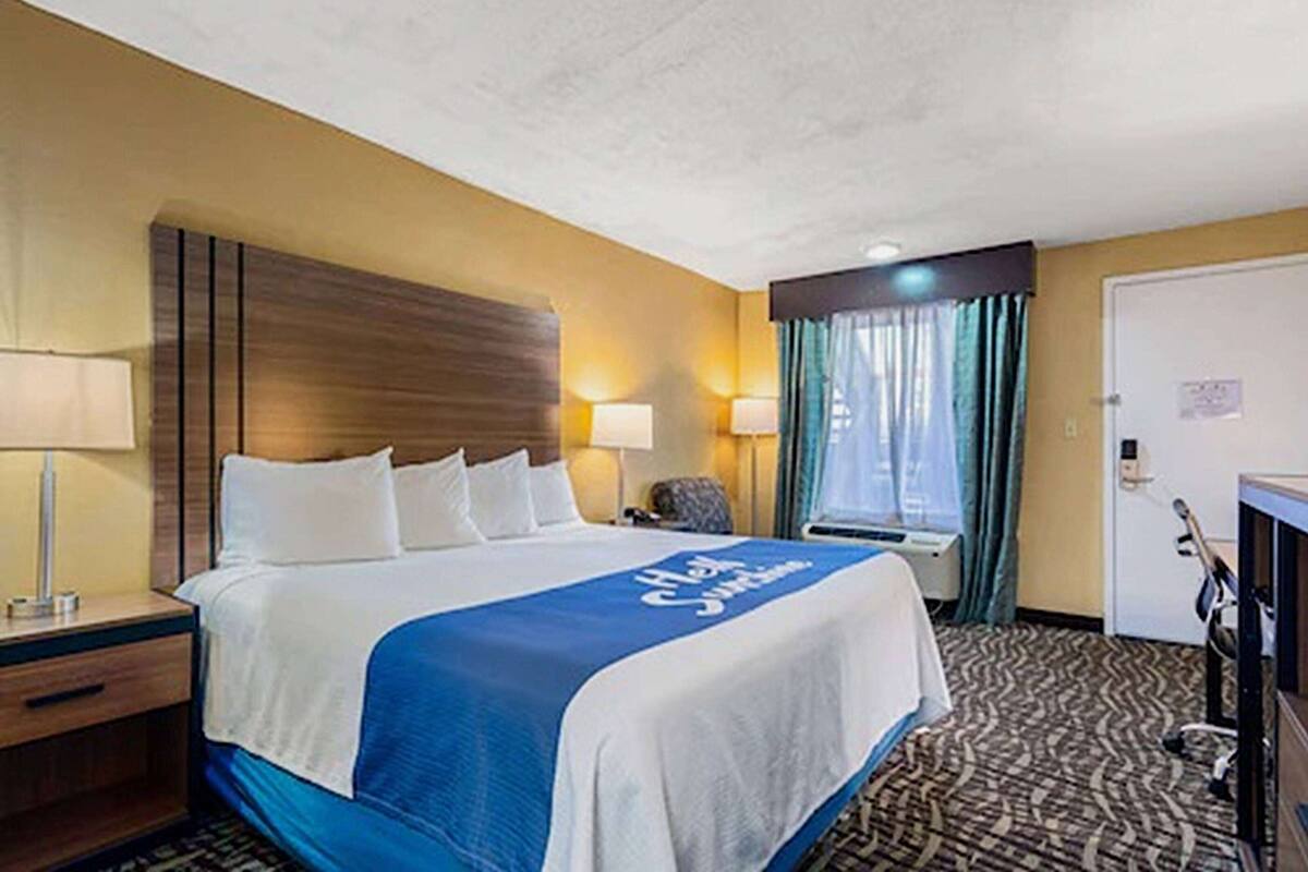 A hotel room with a large bed, two bedside lamps, a desk with a chair, and a door.