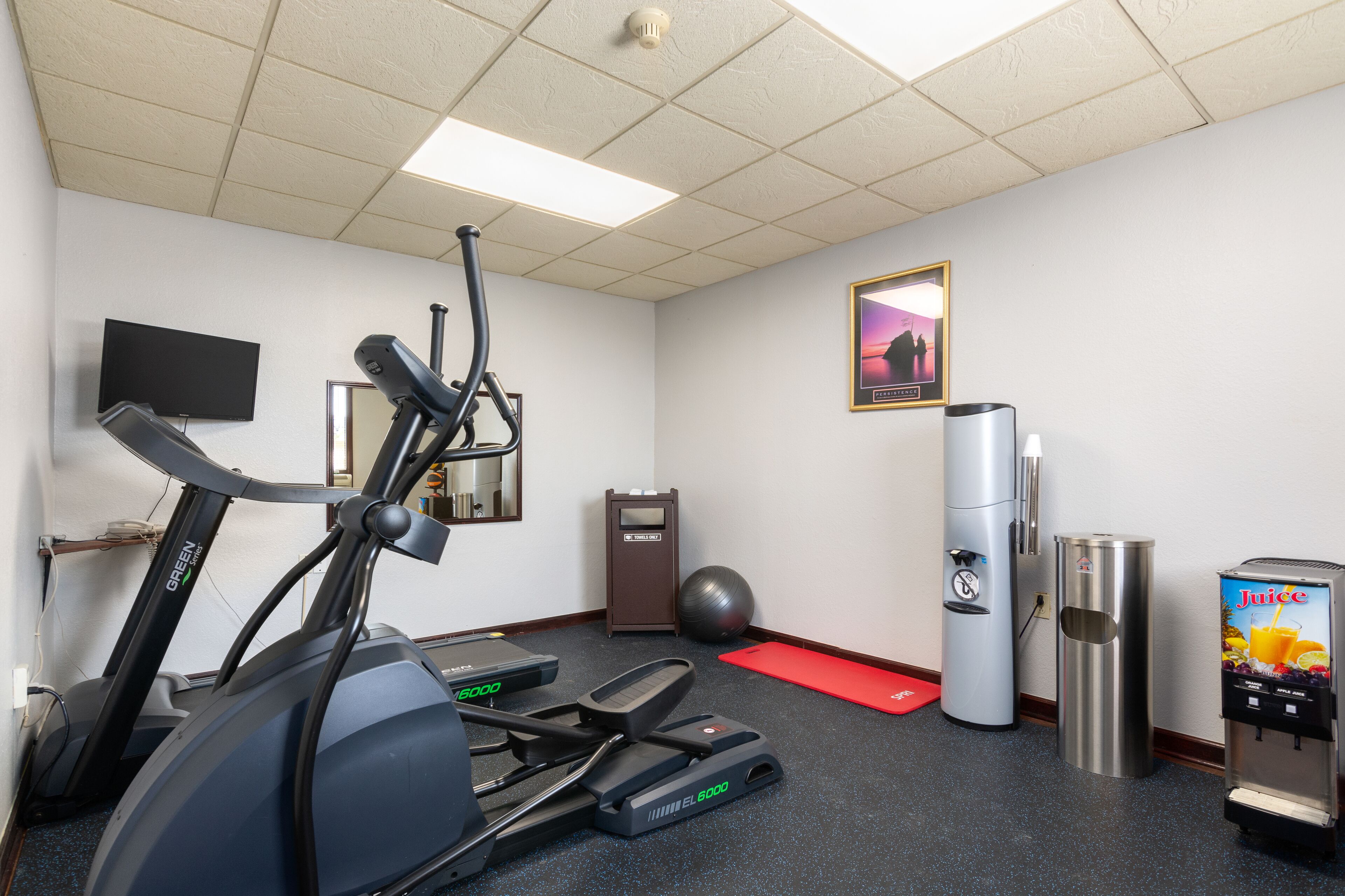 Une salle de remise en forme équipée de matériel d’exercice, d’un distributeur d’eau et d’une poubelle.