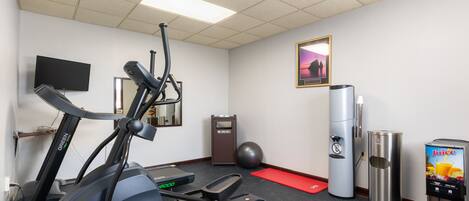 A fitness room with exercise equipment, a water dispenser, and a trash can.