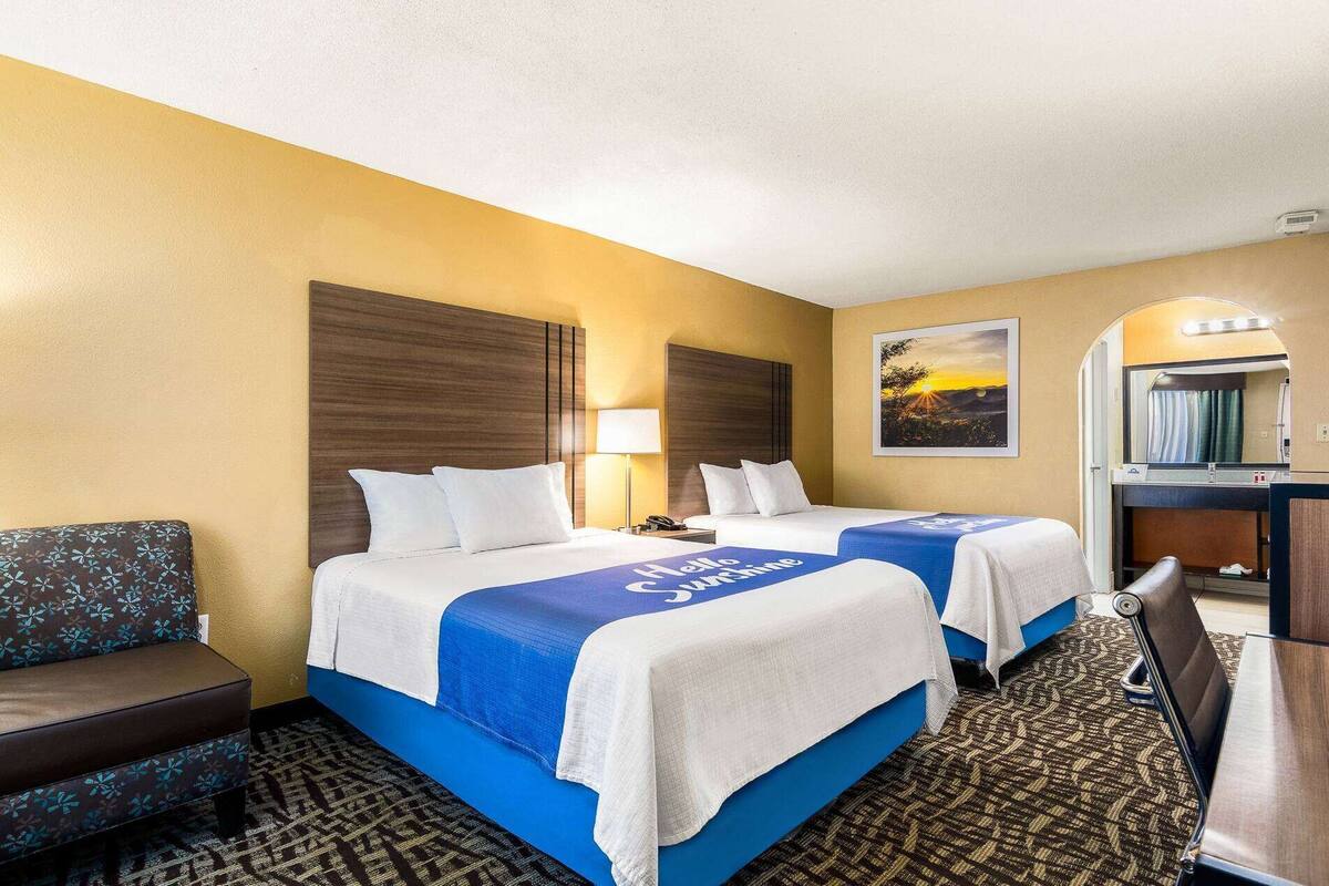A hotel room with two beds, a sofa, a desk, and a bathroom mirror.