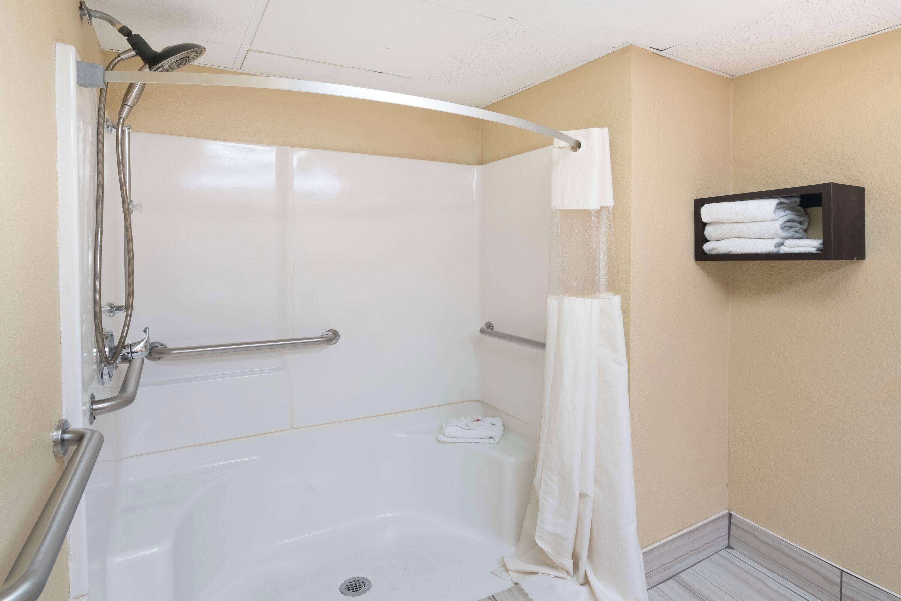 A walk-in shower with a handheld showerhead, grab bars, and a towel rack.