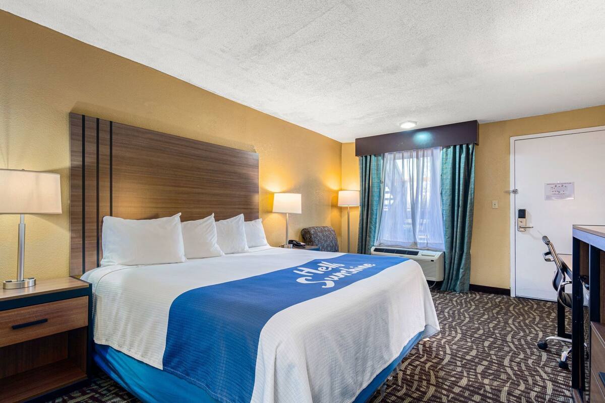 A hotel room with a bed, bedside lamps, a desk, and a window with curtains.