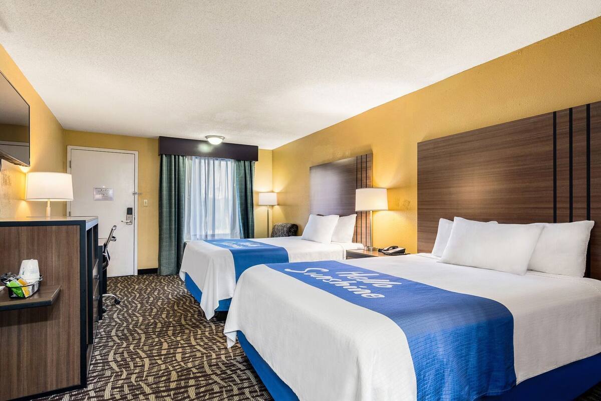 A hotel room with two beds, a desk, a chair, a lamp, and a door.
