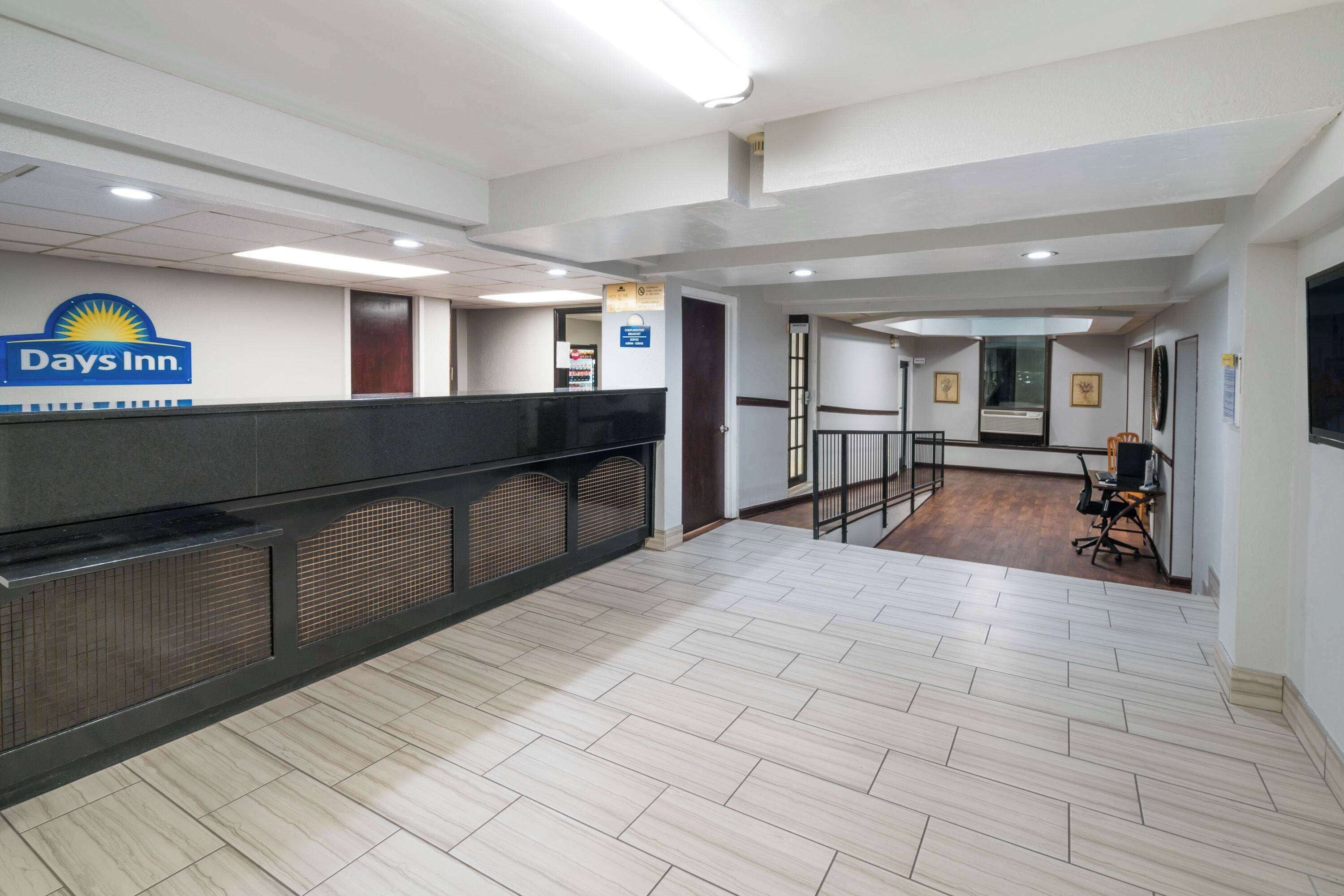 A reception area with a 'Days Inn' sign, a reception desk, a waiting area with chairs, and a wooden floor.