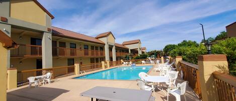 A hotel with a swimming pool, outdoor seating, and balconies.