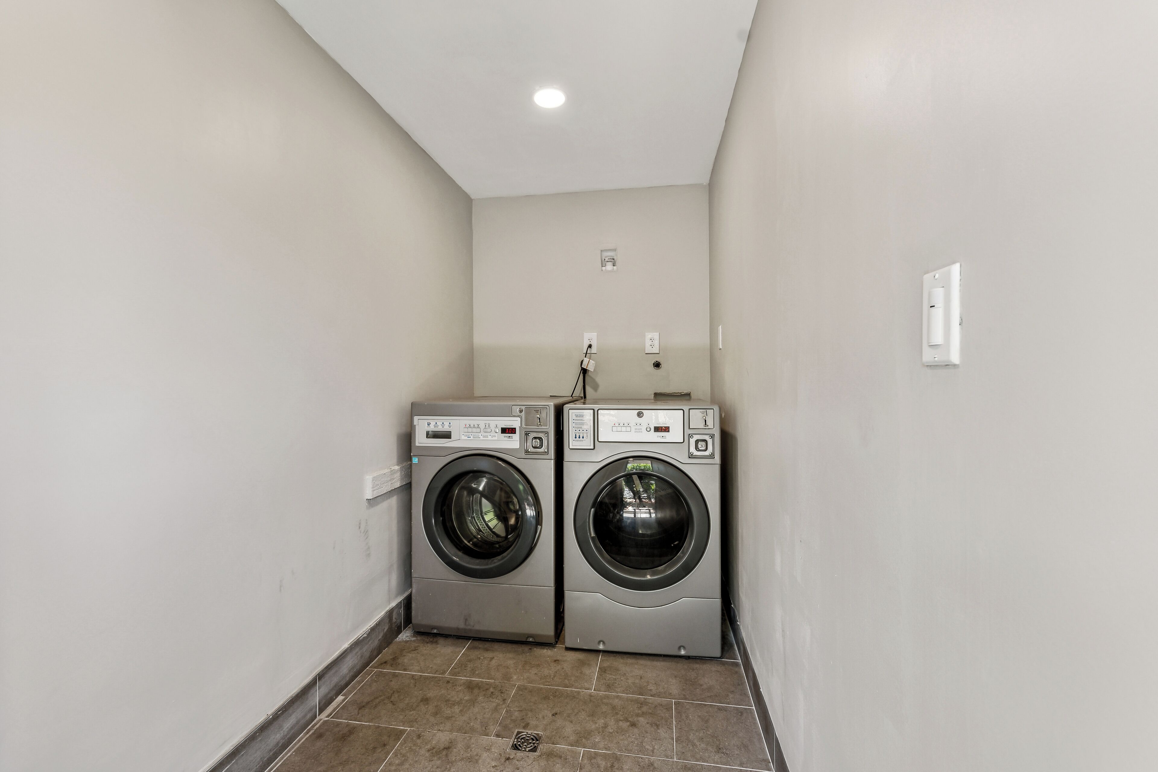 A laundry room with two front-loading washing machines and a wall-mounted dryer.