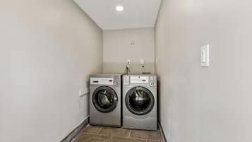 A laundry room with two front-loading washing machines and a wall-mounted dryer.