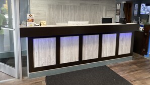 Un mostrador de recepción de diseño moderno, con entrada por puerta de cristal y un mostrador con cartel de prohibido fumar.