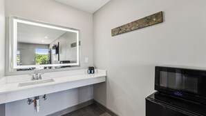 Un baño moderno con un tocador blanco, un espejo grande, un televisor negro y una pared decorativa de madera.