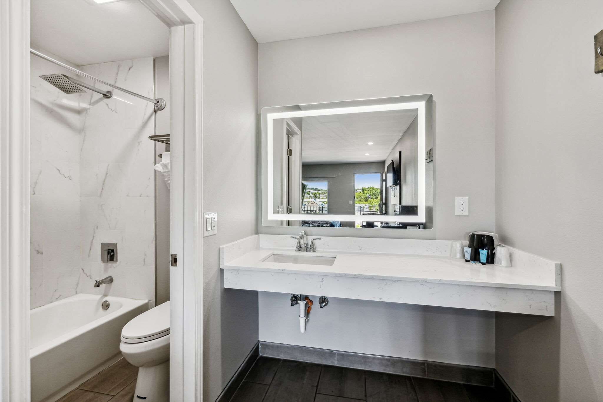 A modern bathroom with a white marble shower, a white sink with a mirror above it, and a toilet.