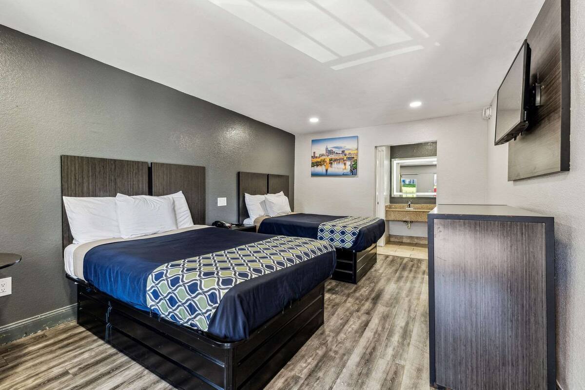 A hotel room with two beds, a desk, and a TV.