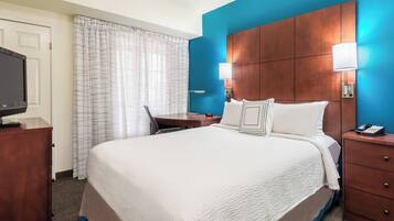 A hotel room with a large bed, a desk, a television, and a nightstand with a phone.