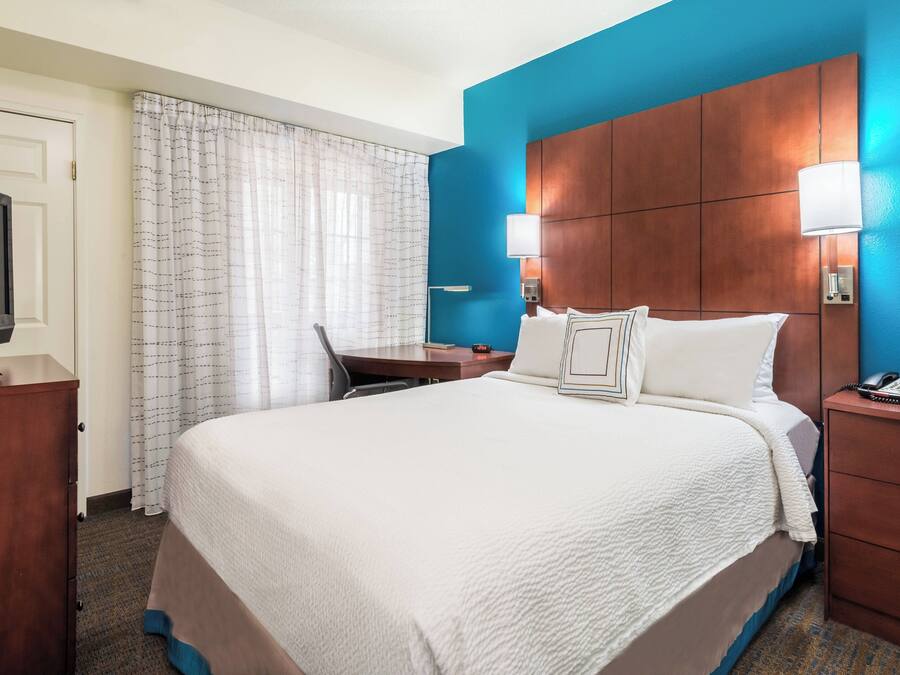 A hotel room with a large bed, a desk, a television, and a nightstand with a phone.