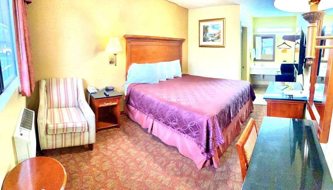 A hotel room with a bed, a chair, a desk, a lamp, and a window.