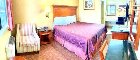 A hotel room with a bed, a chair, a desk, a lamp, and a window.