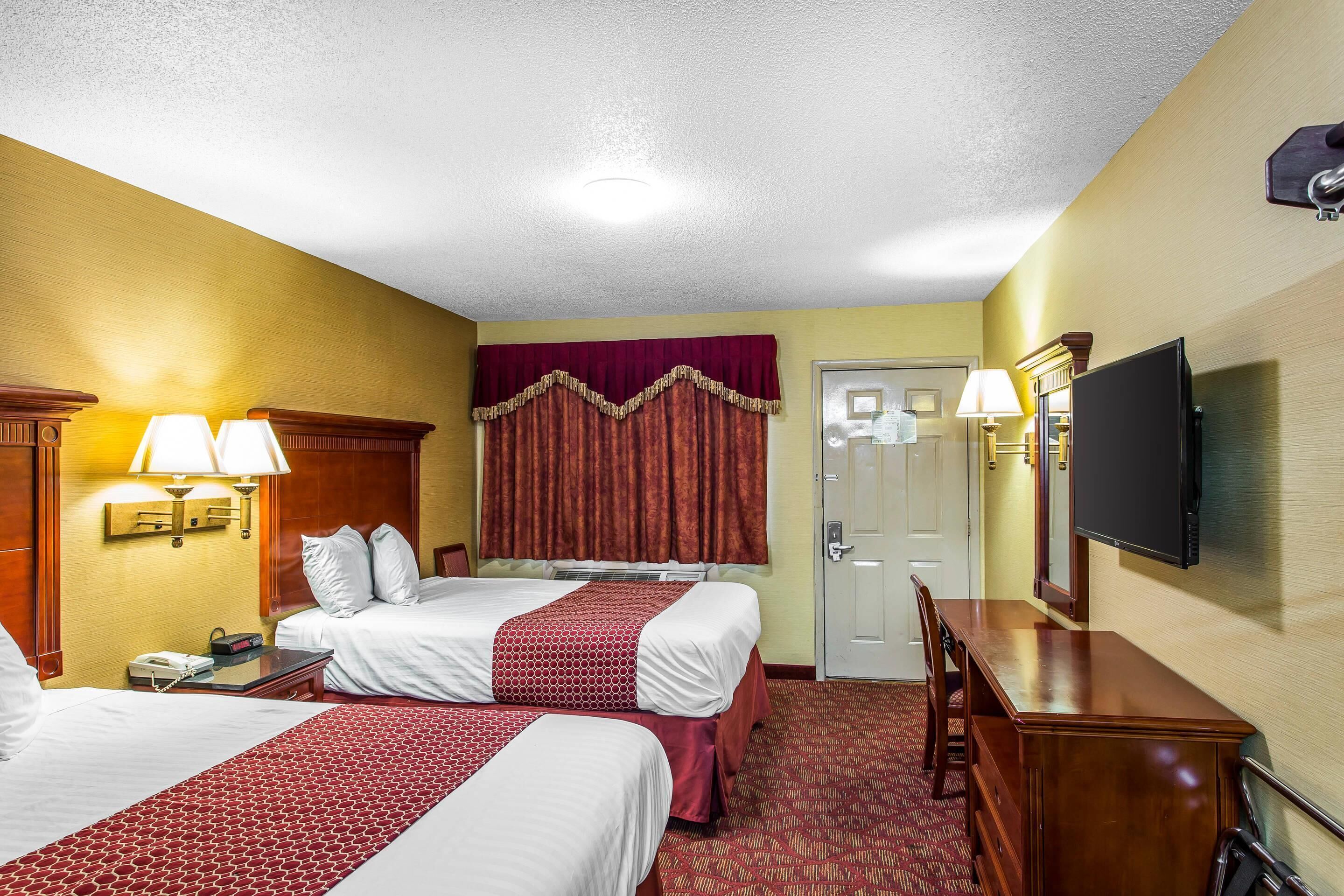 A hotel room with two beds, a desk, a television, and a door.