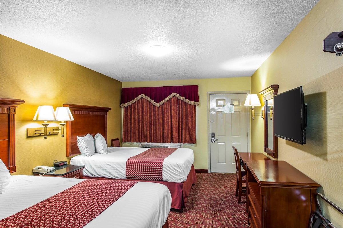 A hotel room with two beds, a desk, a television, and a door.