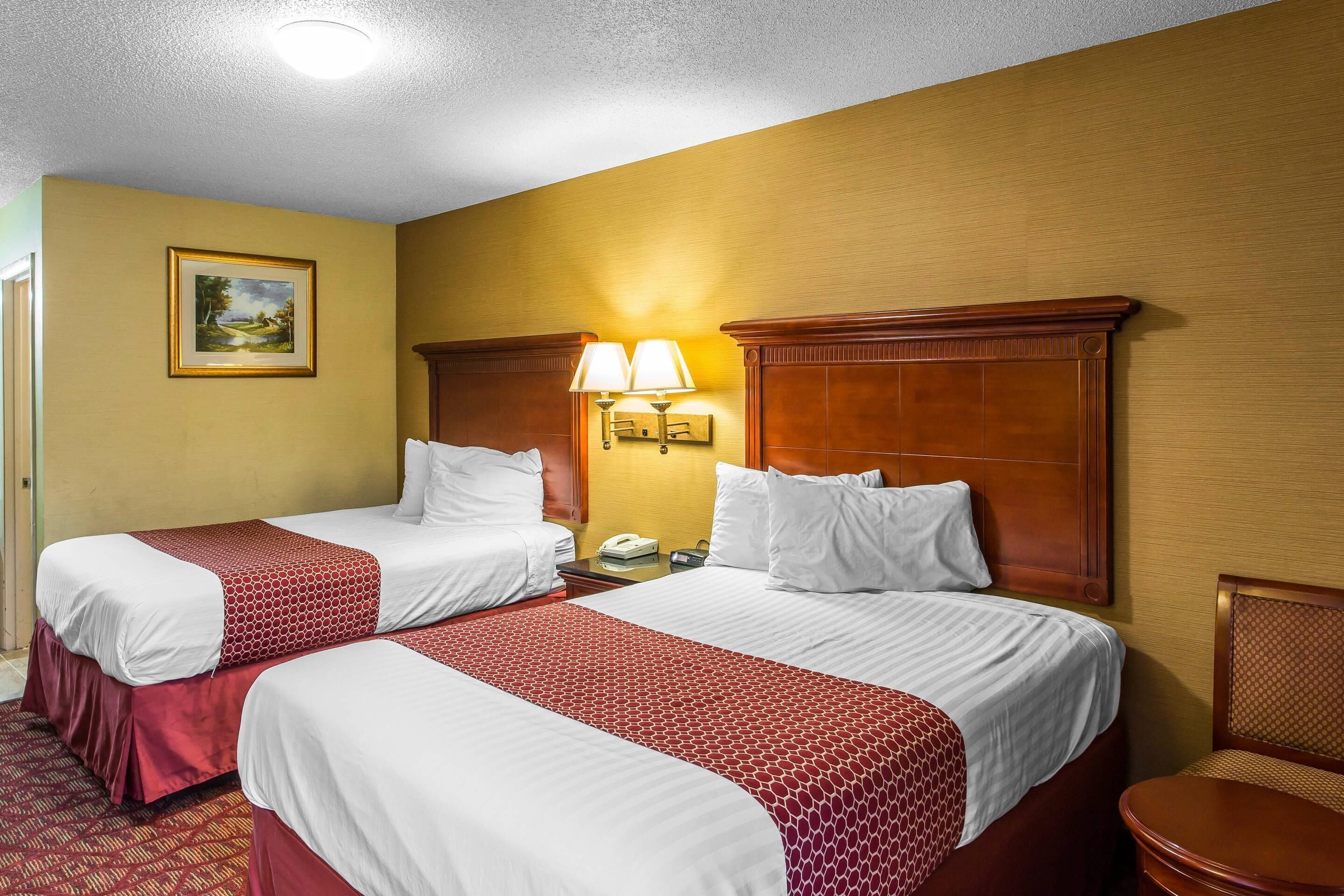 A hotel room with two beds, a nightstand with a lamp, a painting on the wall, and a chair.