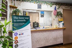 A hotel reception desk with a sign about a rewards program, a clock, an American flag, and a plant.