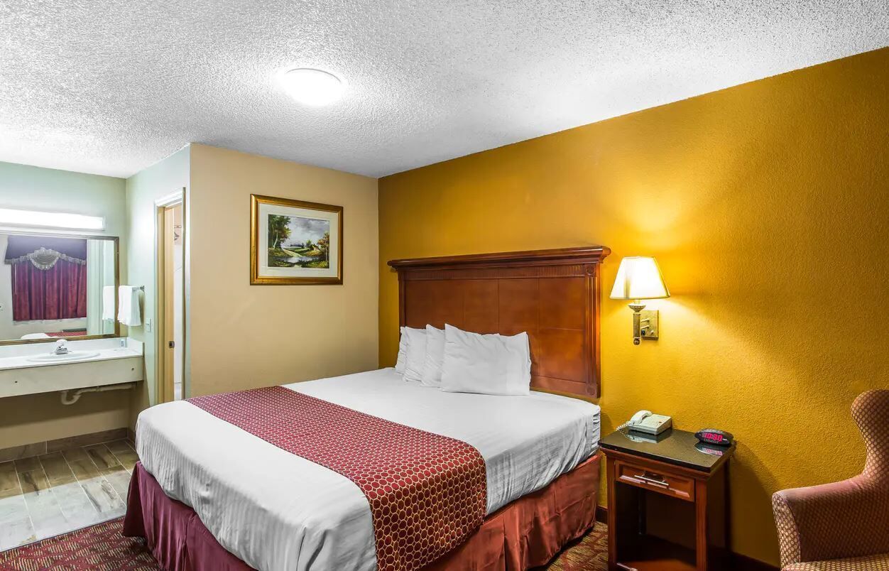 A hotel room with a bed, bedside table, lamp, and a chair.