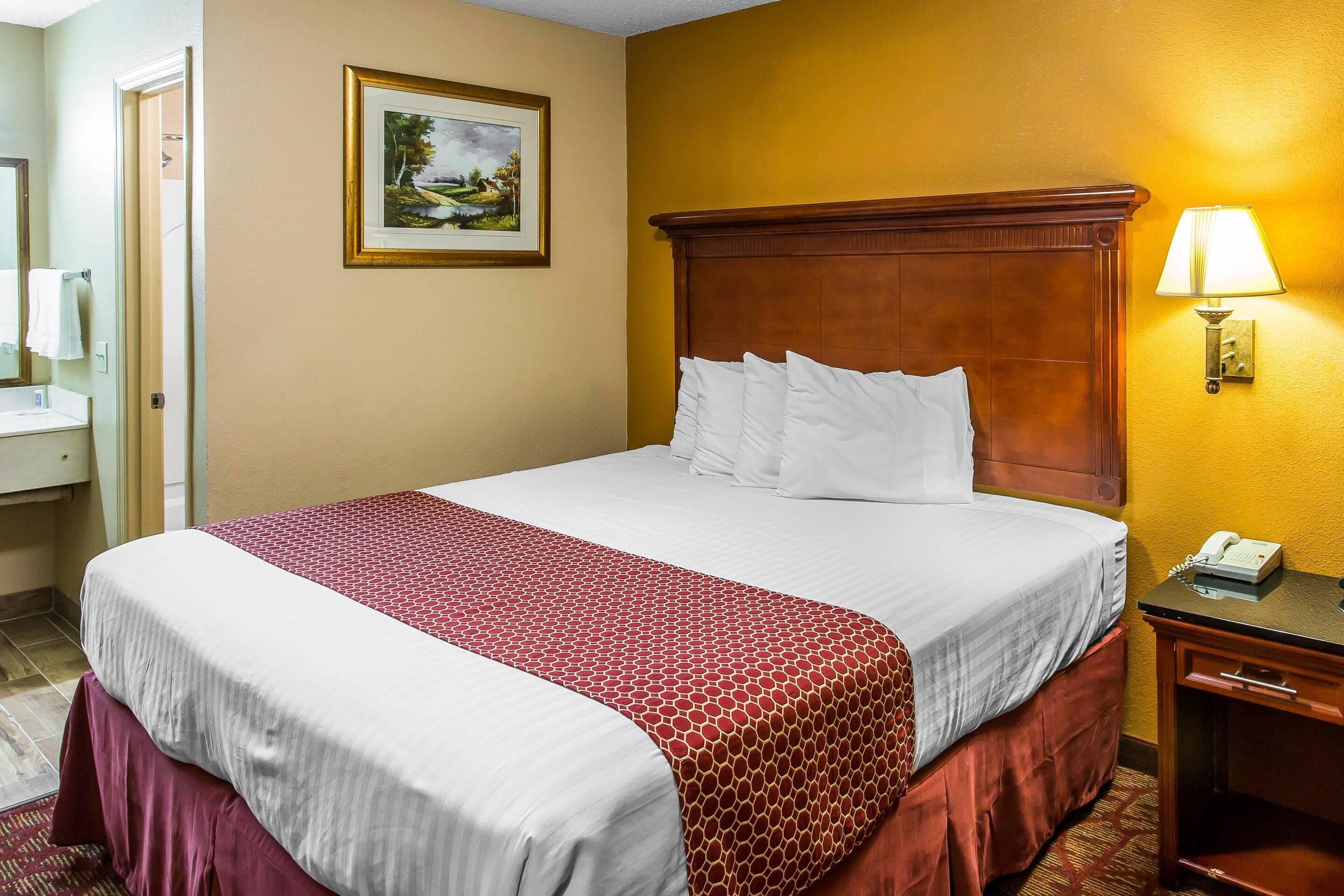 A hotel room with a bed, a bedside table with a lamp, a telephone, and a painting on the wall.