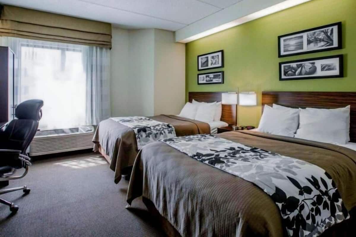 A hotel room with two beds, a desk, and a chair. There are framed pictures on the wall.