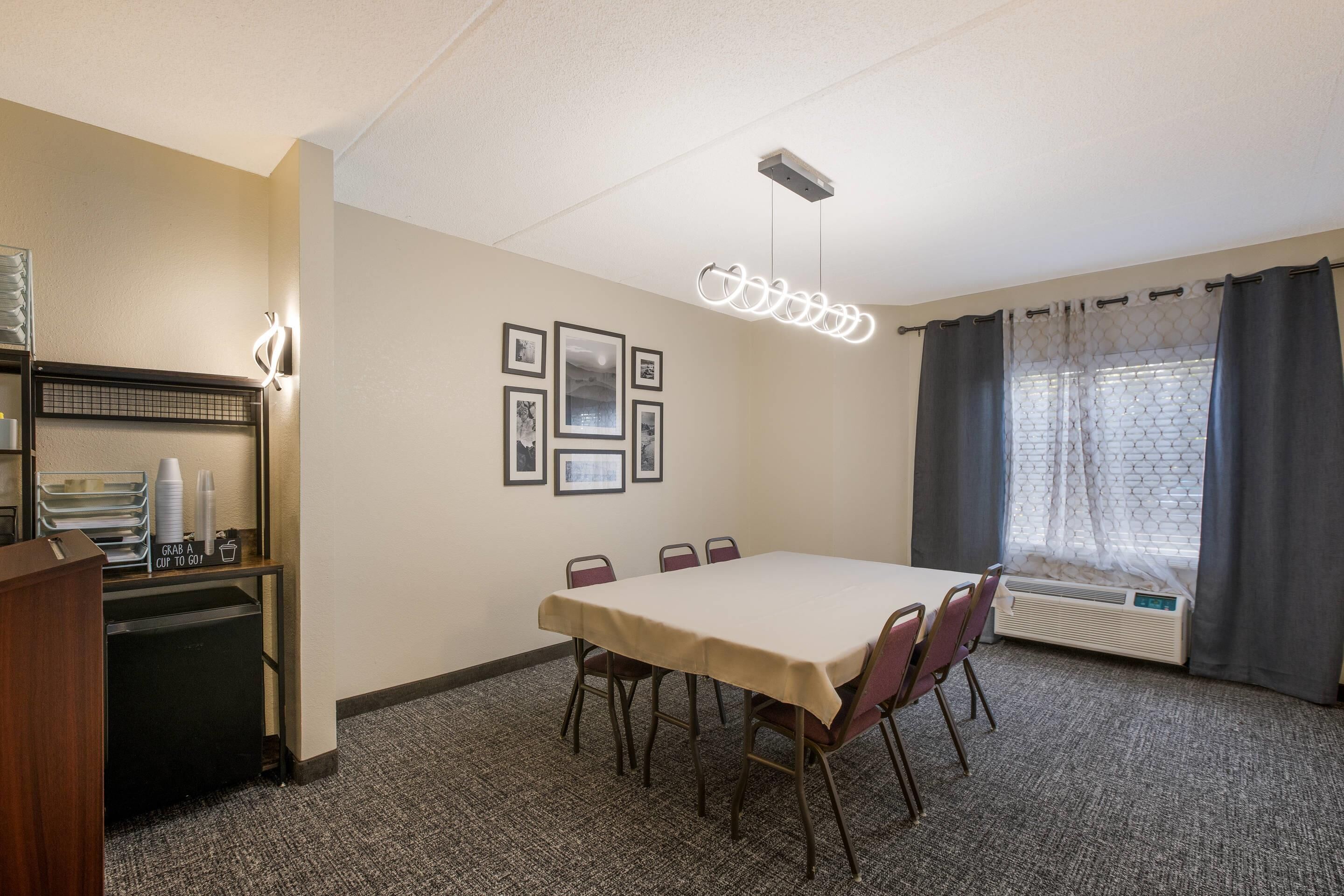 A conference room with a table, chairs, a podium, framed pictures on the wall, and a window with curtains.