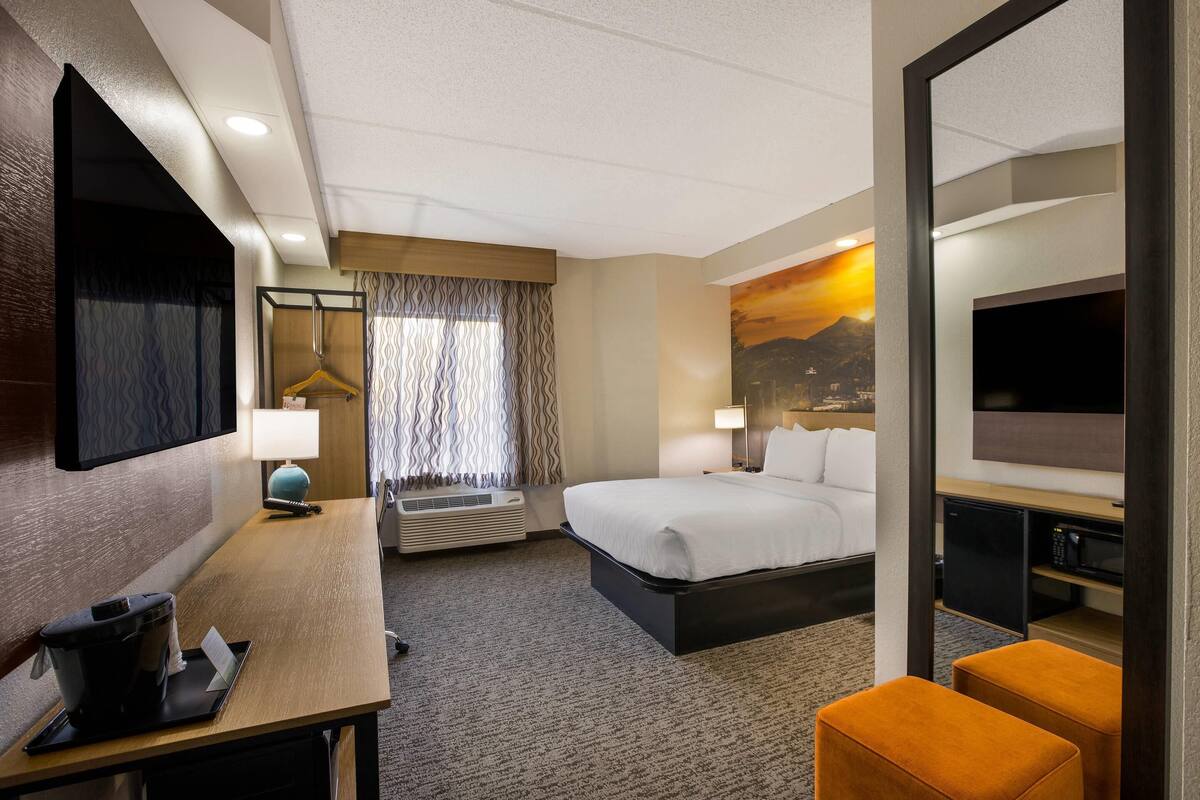 A hotel room with a bed, a desk with a coffee maker, a TV, and a painting on the wall.