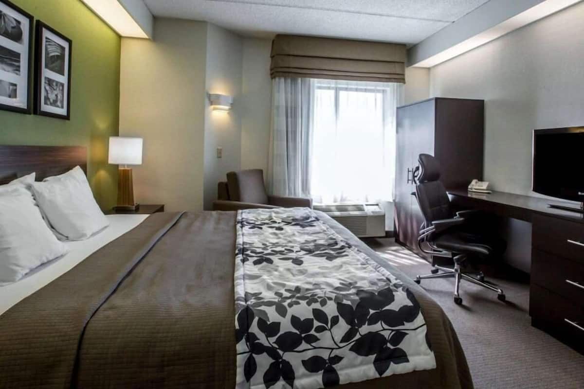 A hotel room with a bed, desk, chair, television, and a window with curtains.