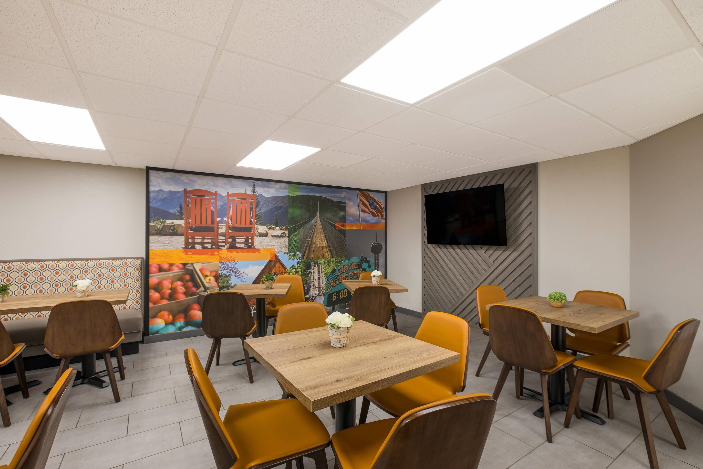 A restaurant with multiple tables and chairs, a mural on the wall, and a flat-screen TV mounted on the wall.
